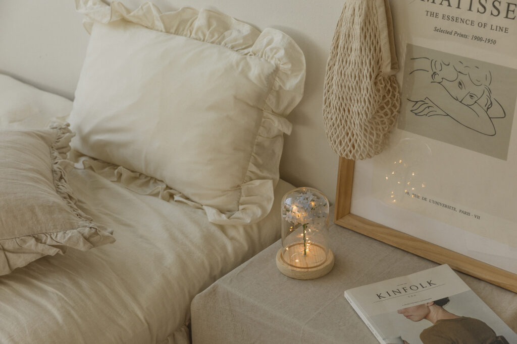 A serene bedroom interior featuring a delicate blue paper flower under a glass dome with fairy lights on a bedside table, creating a calming ambiance.