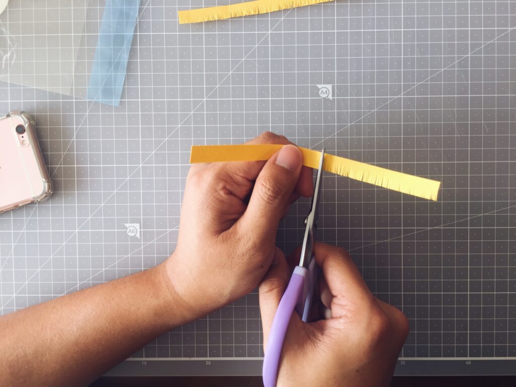 Cutting fine fringes into yellow paper to make the center of a cosmos flower