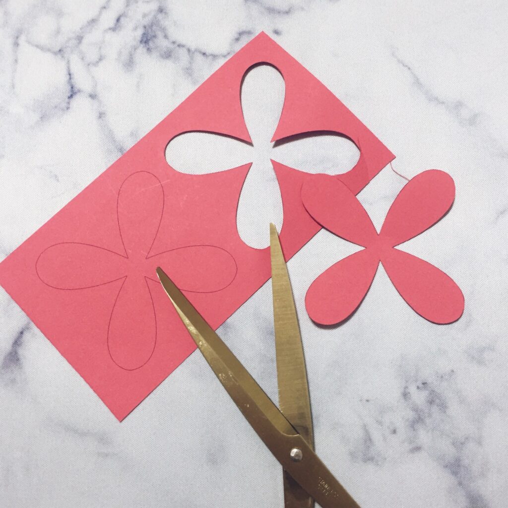 Hands cutting printed cosmos petal shapes from paper with scissors